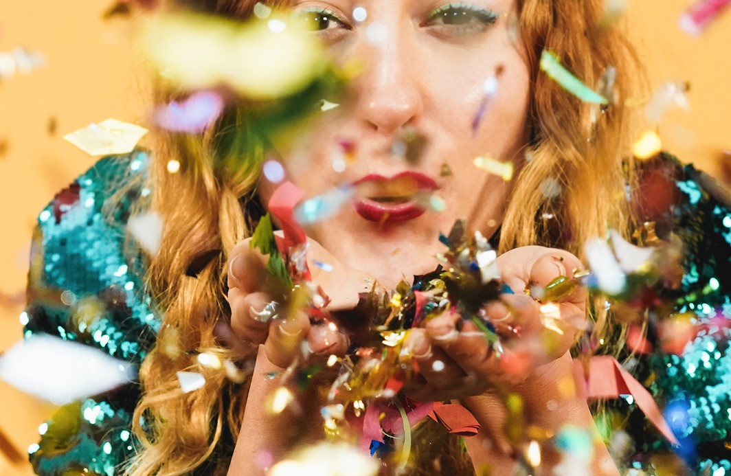 Happy crazy girl blowing confetti with yellow background – Focus on arms