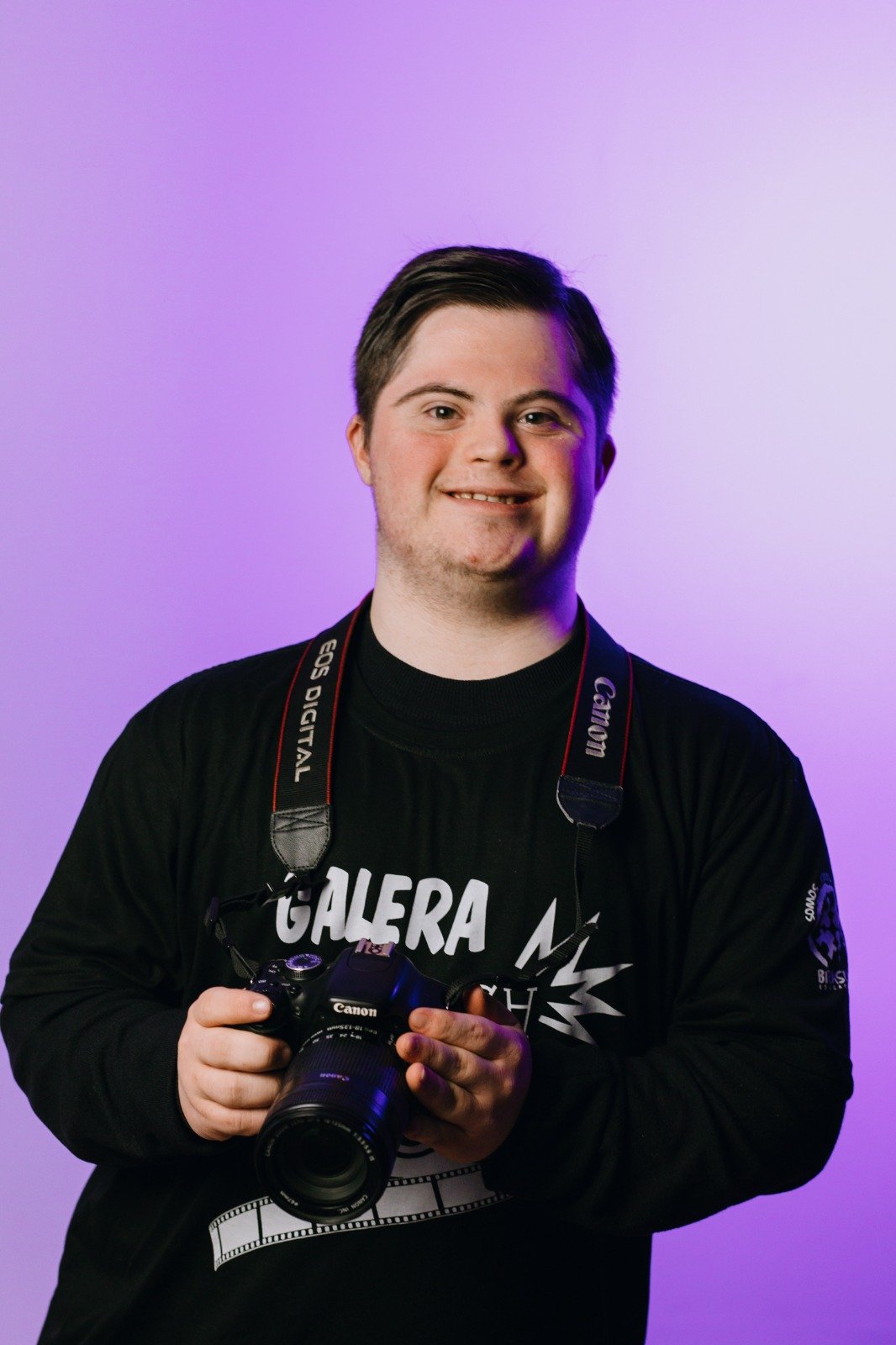 Menino com síndrome de Down segura na altura do peito uma máquina fotográfica.