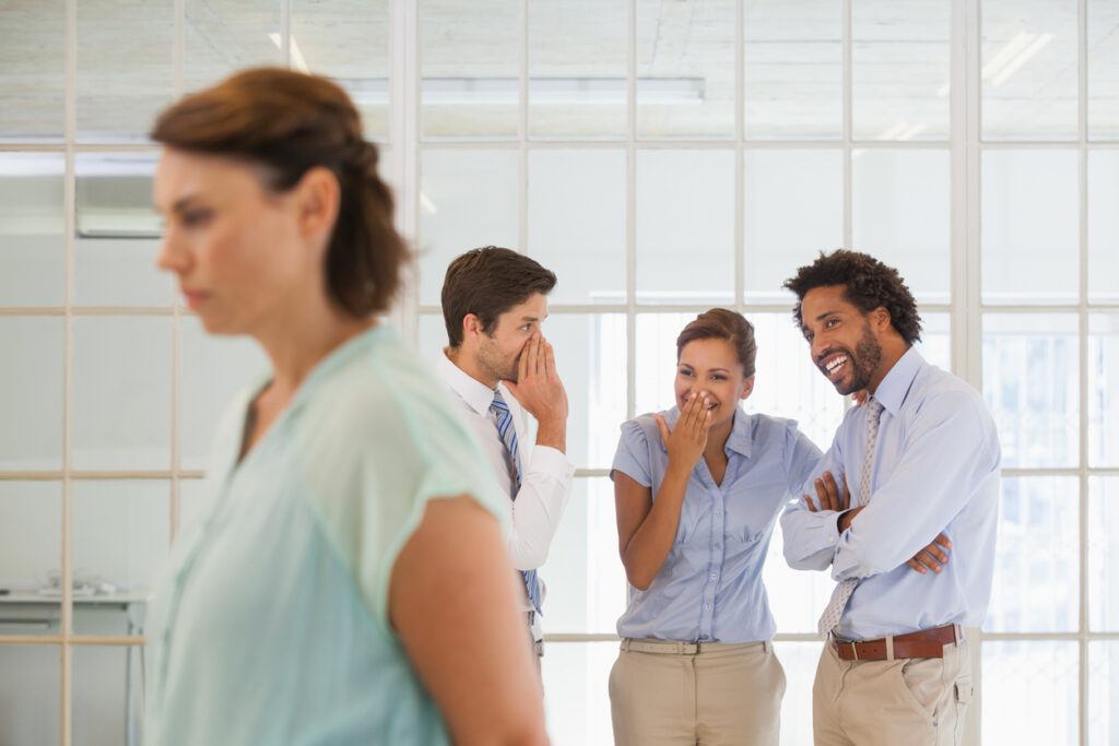 Colleagues gossiping with sad businesswoman in foreground