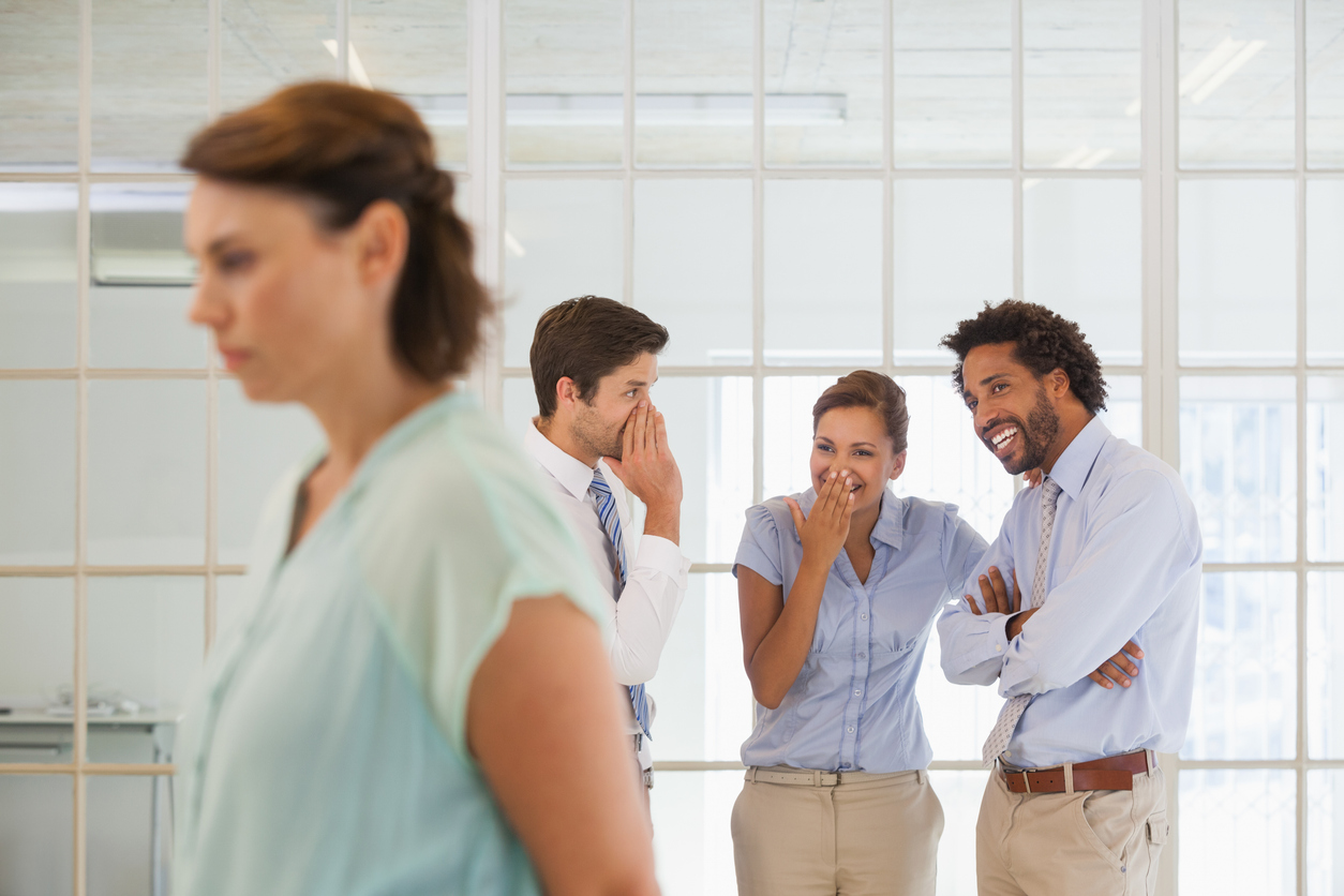 Colleagues gossiping with sad businesswoman in foreground