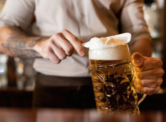 closeup-de-barman-removendo-espuma-de-cerveja-enquanto-despeja-cerveja-em-um-pub_637285-2954