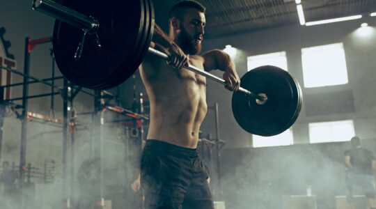 Fit young man lifting barbells working out in a gym