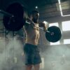 Fit young man lifting barbells working out in a gym