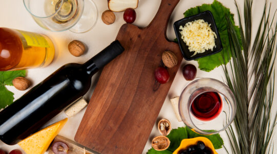 top-view-red-wine-white-wine-with-olive-walnut-grape-cutting-board-shredded-parmesan-cheese-white-table-decorated-with-leaves