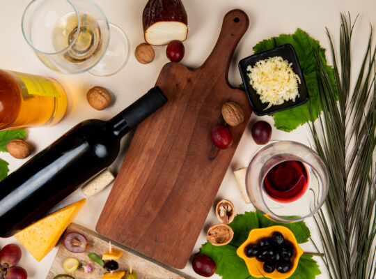 top-view-red-wine-white-wine-with-olive-walnut-grape-cutting-board-shredded-parmesan-cheese-white-table-decorated-with-leaves