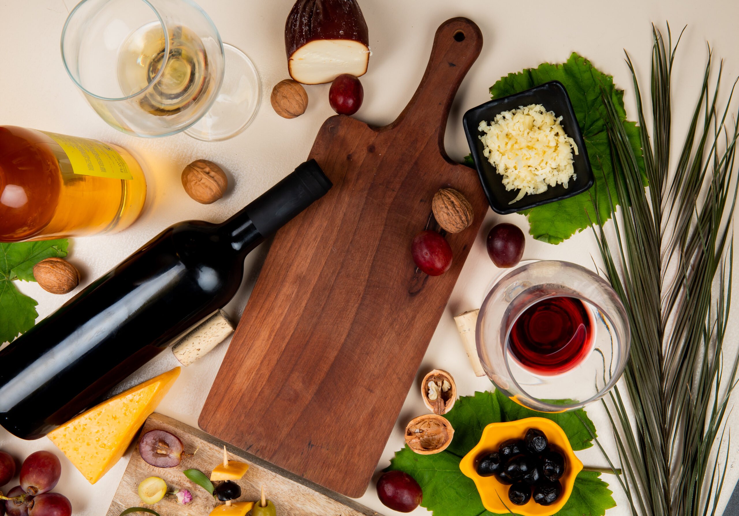 top-view-red-wine-white-wine-with-olive-walnut-grape-cutting-board-shredded-parmesan-cheese-white-table-decorated-with-leaves
