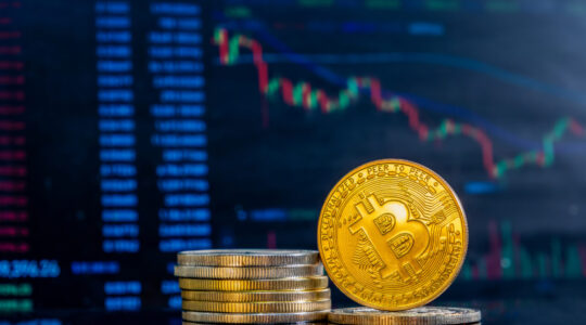 Close-up of golden Bitcoins on a dark reflective surface and the histogram of decreasing crypto in the background