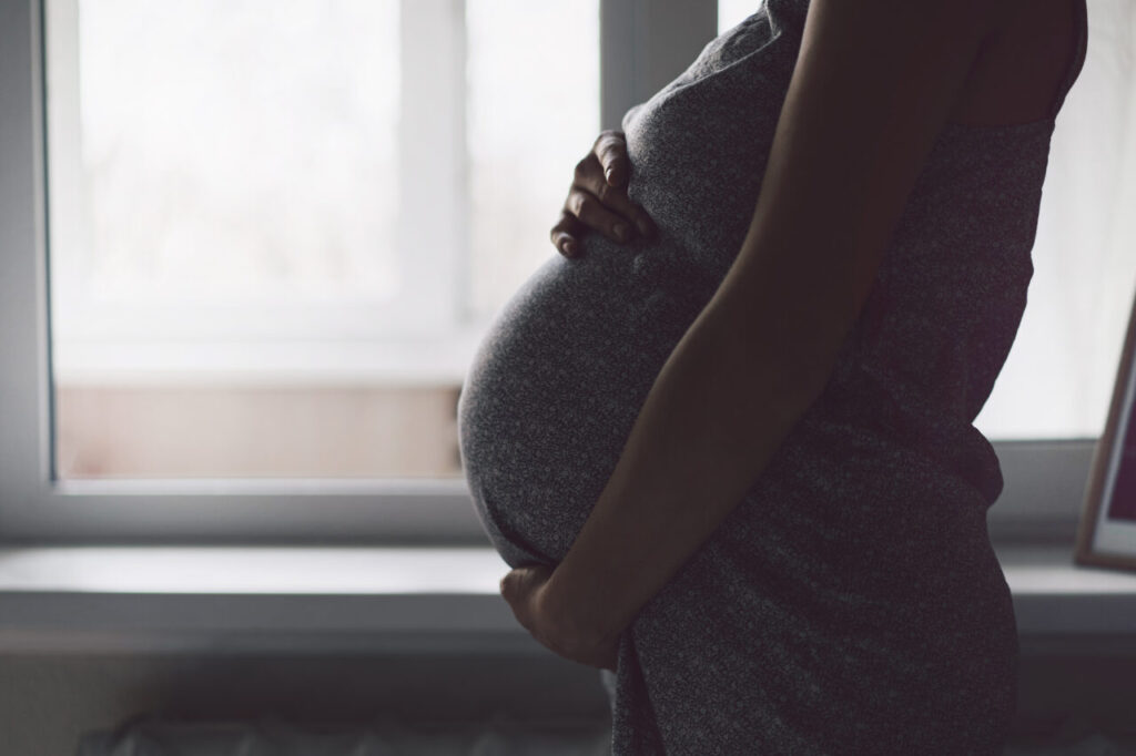 Happy Attractive pregnant woman standing near the window and holding her belly.