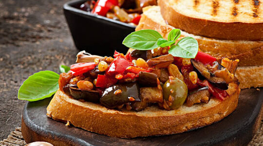 Bruschetta caponata with raisins and pine nuts decorated with a leaf of basil