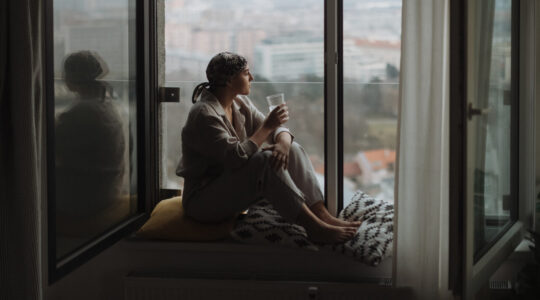 Young unhappy woman with cancer sitting in a window and looking at view.