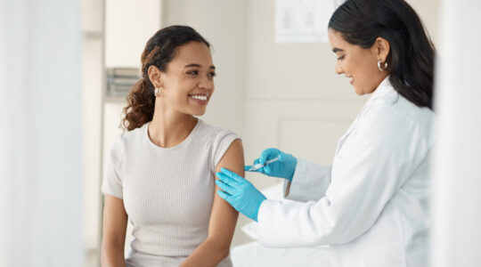 Injection, vaccine and patient at the clinic for consulting and help with prevention with a smile. Doctor, inject and woman on arm for virus with gloves in medical room for wellness or health.