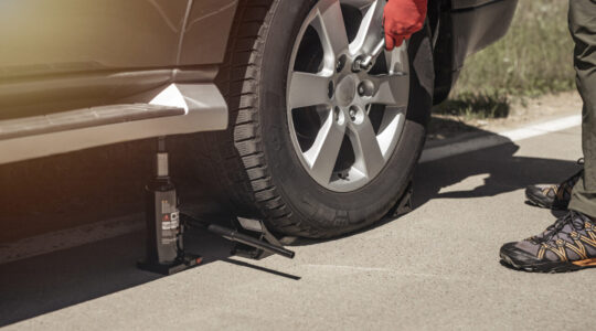 Hydraulic car jack is put under auto by hands in gloves, close up