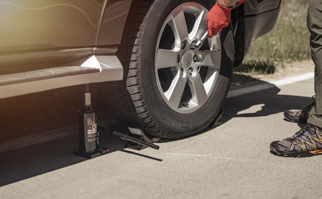Hydraulic car jack is put under auto by hands in gloves, close up