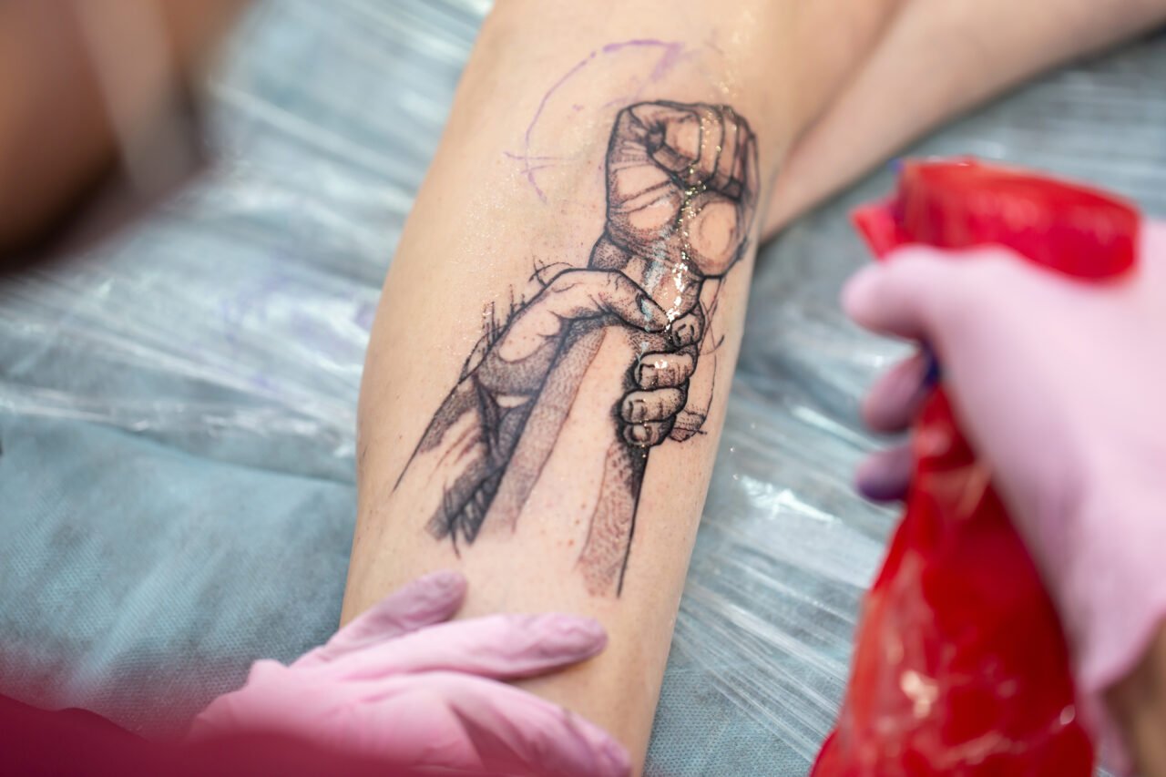 Tattoo master professional application of alcohol on the skin of clients