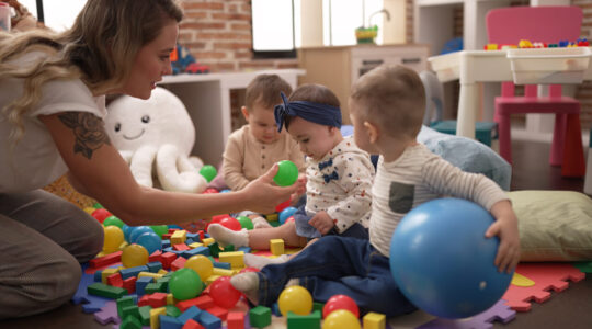 Teacher and preschool students playing with balls sitting on floor at kindergarten