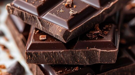 Dark chocolate bars stacked on marble with cocoa nibs