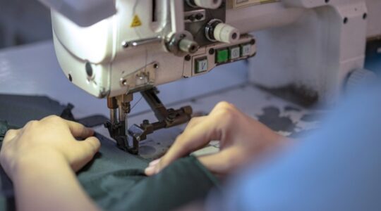 Hands of young Asian woman using sewing machine in workshop.