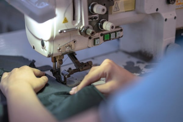 Hands of young Asian woman using sewing machine in workshop.