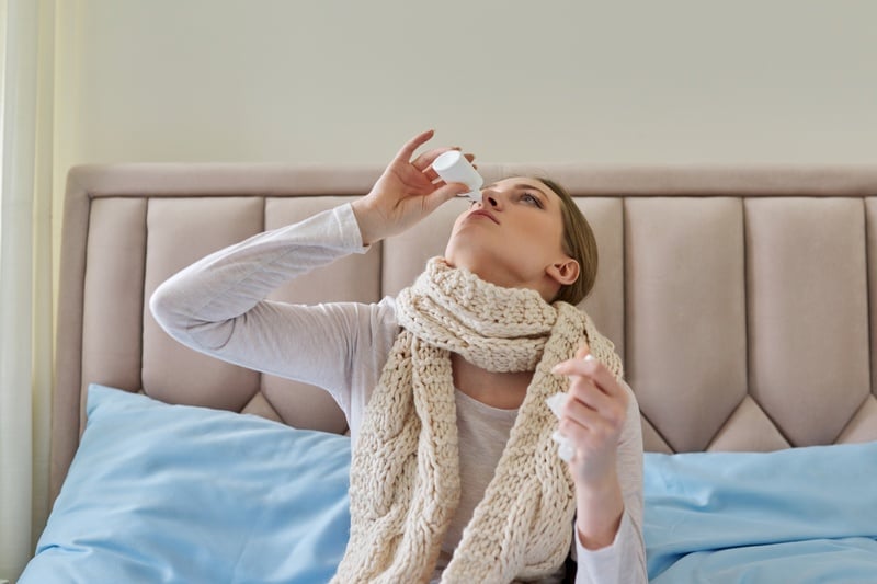Sick woman at home in bed using nasal drops