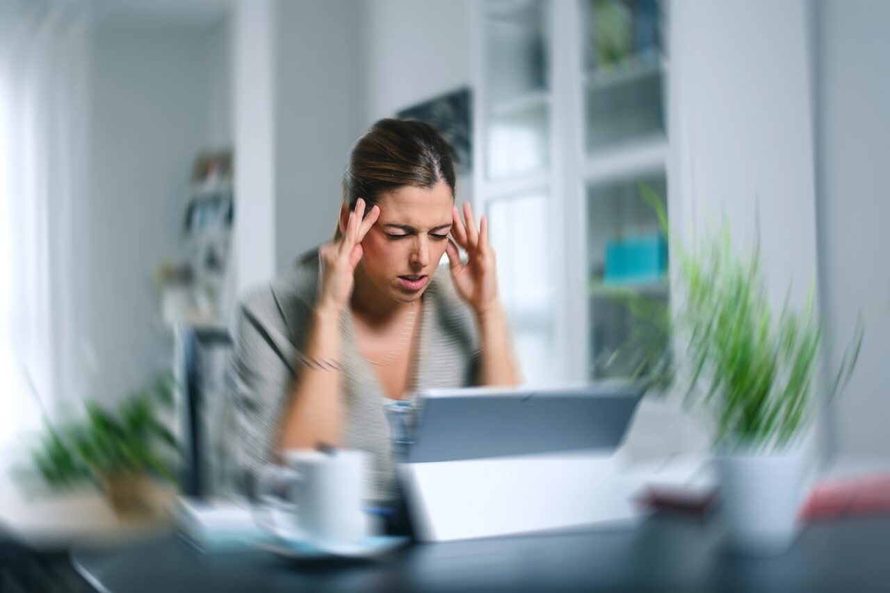 Sick dizzy young woman suffering headache while working on her laptop at home.