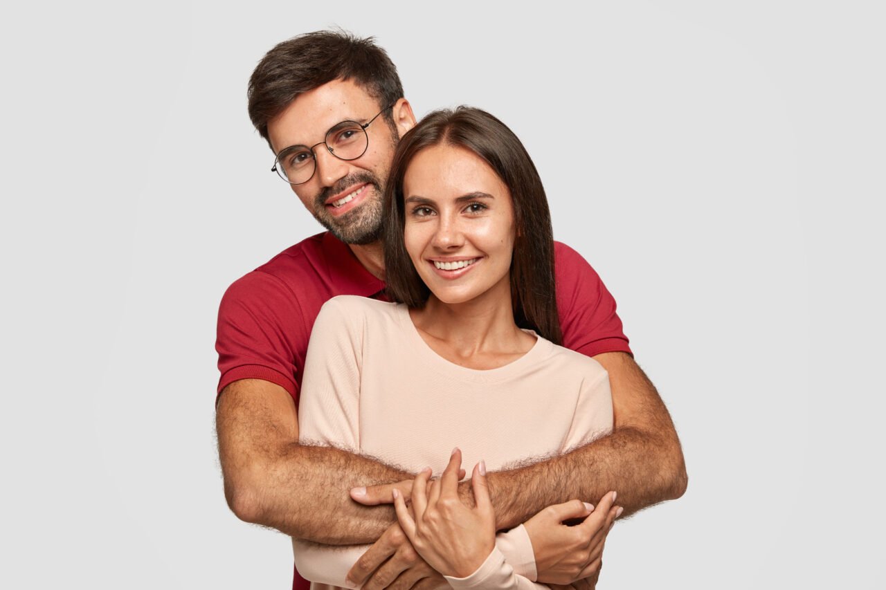 Lovely couple have warm cuddle, pose for family portrait, smile joyfully, have good relationships. Affectionate brother embraces his sister isolated over white wall. Girlfriend and boyfriend have date
