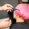 Hands of hairdresser combing hair making short pink hairstyle for a young caucasian woman in a beauty salon.