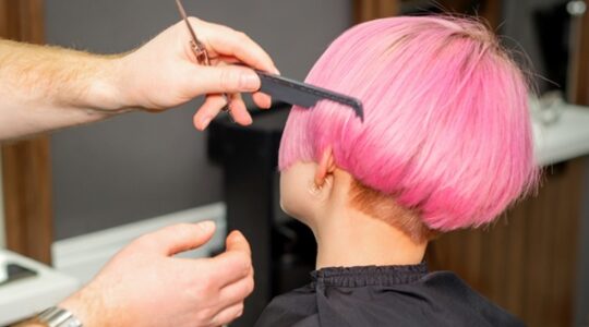 Hands of hairdresser combing hair making short pink hairstyle for a young caucasian woman in a beauty salon.