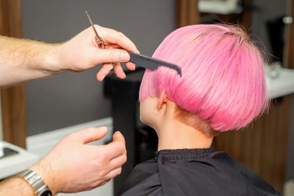 Hands of hairdresser combing hair making short pink hairstyle for a young caucasian woman in a beauty salon.