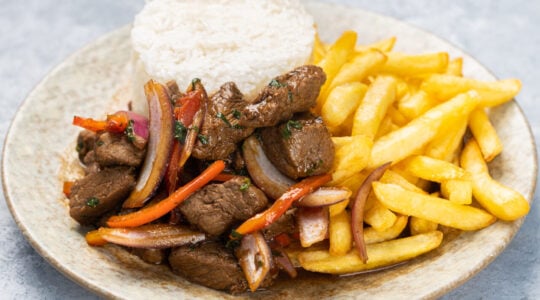 Closeup of roasted meat with sauce, vegetables and fries in a plate on the table