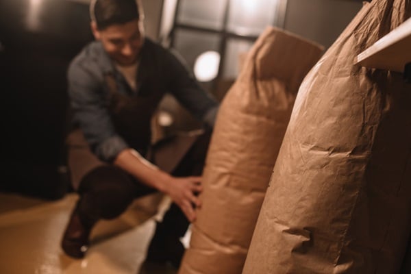 worker in apron with paper bags of coffee beans