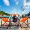 Woman with hat sitting on chairs beach in beautiful tropical bea