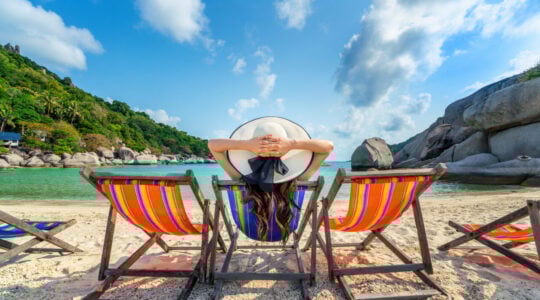 Woman with hat sitting on chairs beach in beautiful tropical bea