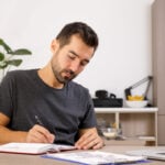 Man writing on notebook at his desk.