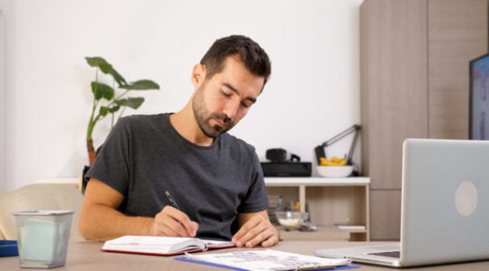 Man writing on notebook at his desk.