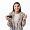 Cheerful young woman winning money on phone, achieve goal in smartphone app, holding mobile phone horizontally and say yes, white background
