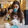 Beautiful woman is holding her cute dog, drinking coffee in cafe