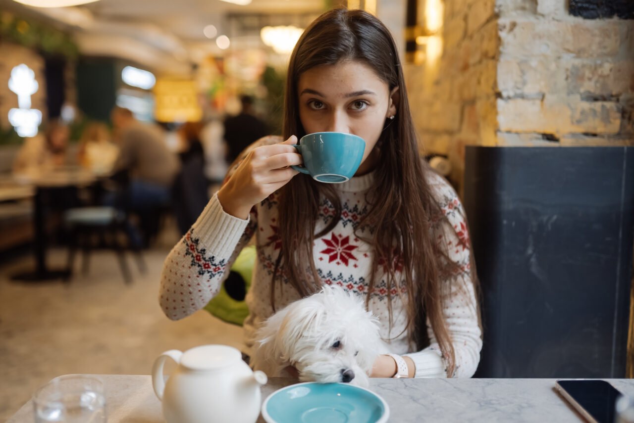 Beautiful woman is holding her cute dog, drinking coffee in cafe