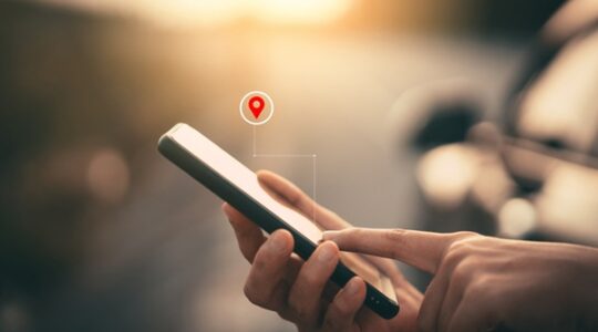 Woman hand using smart phone with navigator location point at street background. Technology interenet and travel adventure concept.