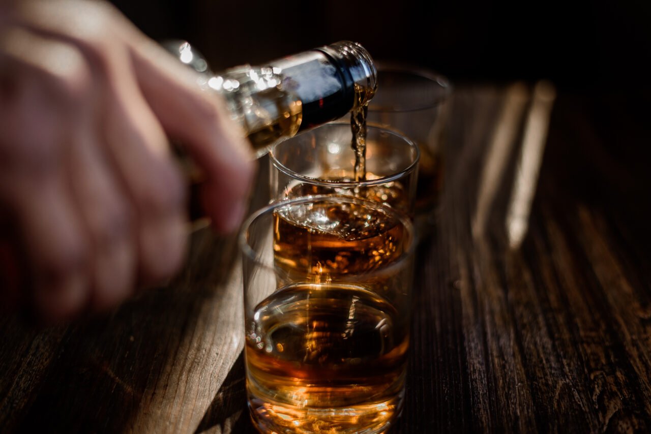 Pouring strong alcohol drink into the glasses which are on the w