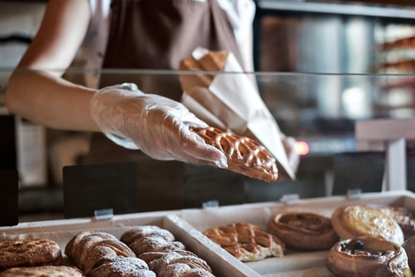 European woman sells in bakery putting bread in paper bag.