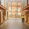 Retail Warehouse full of Shelves with Goods in Cardboard Boxes, Female Worker Checks and Sorts Packages for Delivery. Distribution Logistics Center.