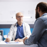 Old physician listens to man in clinic