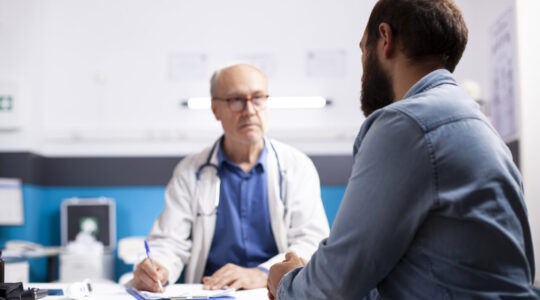 Old physician listens to man in clinic